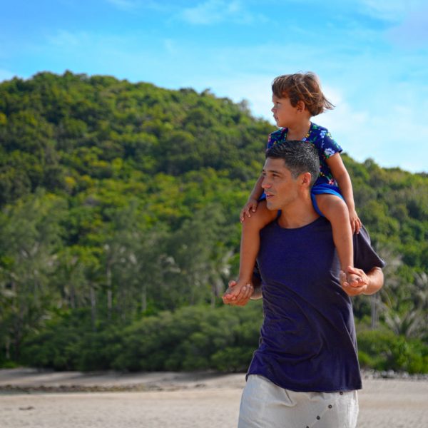 A father with his son on his shoulders walking at the beach in one of the best international places to travel with toddlers