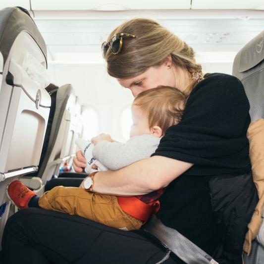 A mother and her toddler sitting together in an airplane seat.